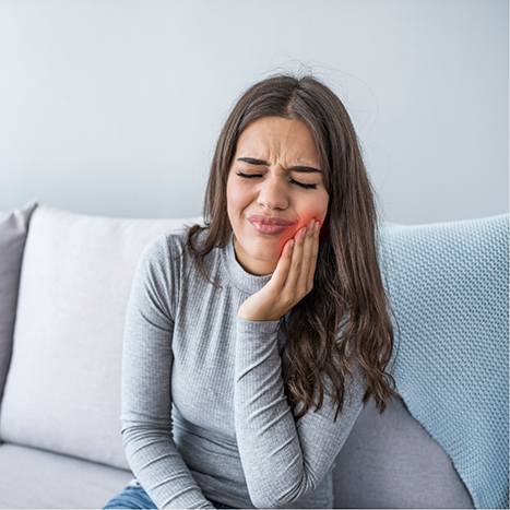 Woman holding her cheek in pain before seeing an emergency dentist in Rogers