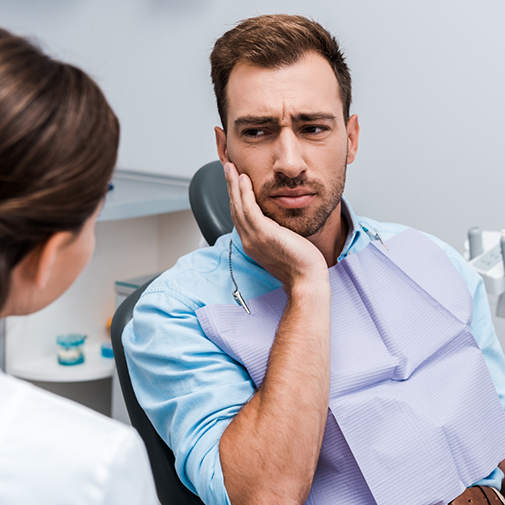 Man holding his cheek in pain while talking to his emergency dentist