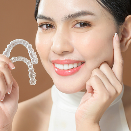 Smiling woman holding two Invisalign aligners