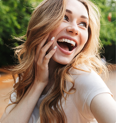 Woman with wavy blonde hair smiling and touching her face